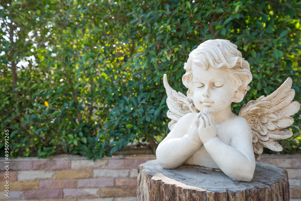 White cute cupid statue in garden with green tree background. Love valentine day concept. White cute cupid statue in garden with green tree background. Love valentine day concept.