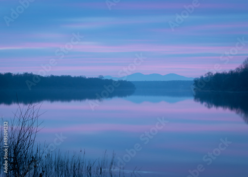 Peaceful atmospheric landscape with pastel colors  Sava river at twilight  forested banks lead to distant mountain silhouette in haze  calm nature and water reflection