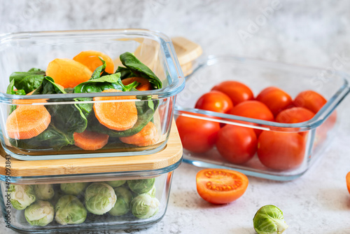 Fototapeta Naklejka Na Ścianę i Meble -  Various vegetables in glass containers: carrots, spinach, tomatoes, Brussels sprouts. Vegan food and snacks in containers, gray background. Clean eating, raw food, detox