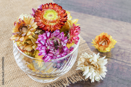Dried straw flower heads in cup on wooden background.