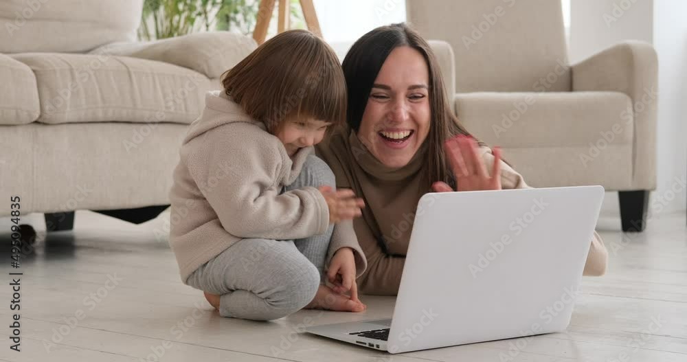 Joyful mother with daughter waving hand and greeting while watching laptop at home Joyful mother with daughter waving hand and greeting while watching laptop at home