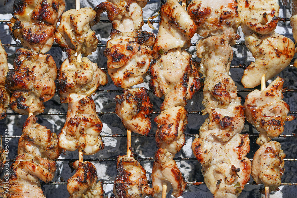 Grilling shashlik on barbecue grill. Skewered chicken satay roasted on smoky charcoal grill