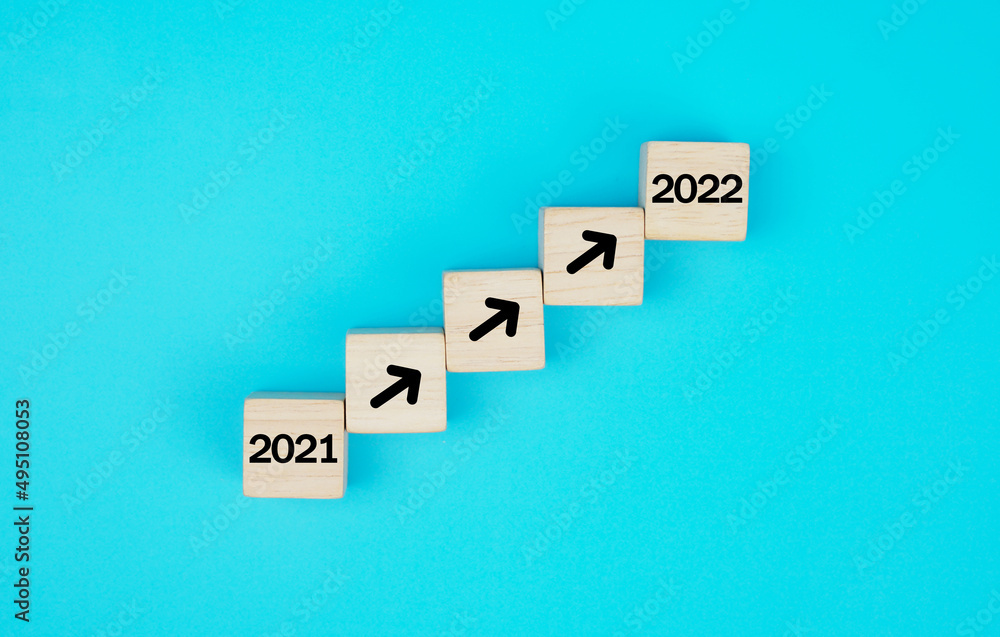Obraz premium Wood block stacking as step stair. business growth success process with arrow moving up from year 2021 to 2022, on blue background. 