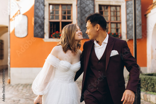 An international wedding couple, a European bride and an Asian groom walk around the city together.