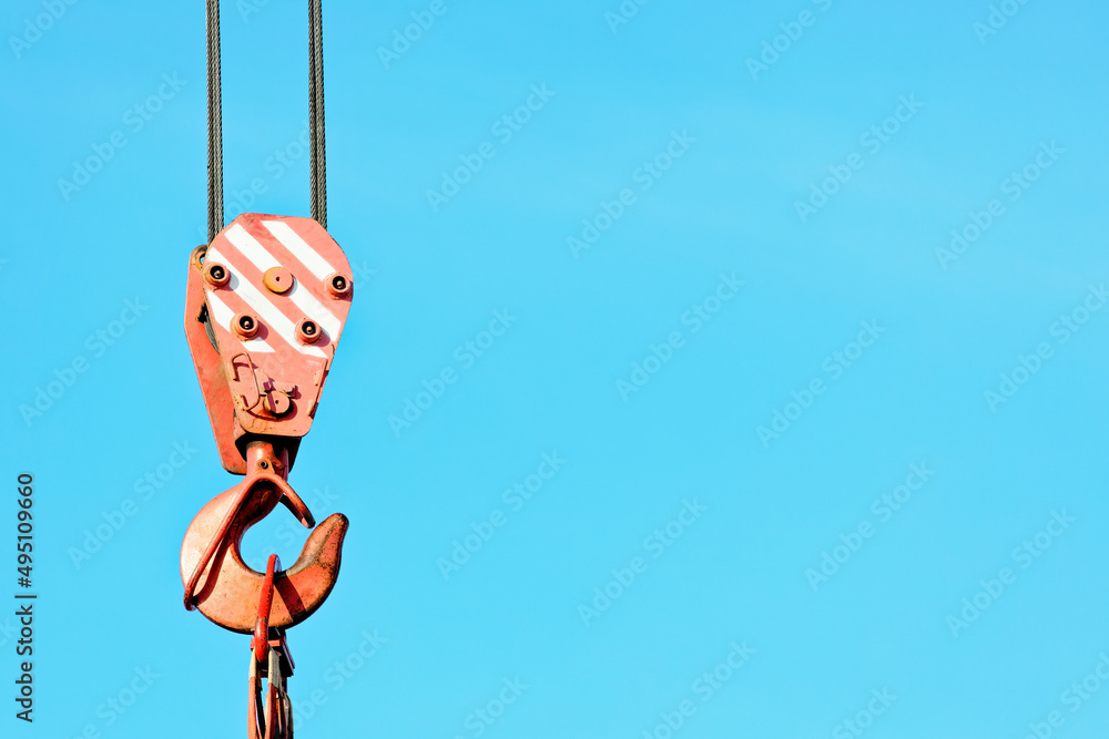 Crane hook with metal cable against blue sky. Unloading or loading of goods. Background with space to copy. Crane hook with metal cable against blue sky. Unloading or loading of goods. Background with space to copy.