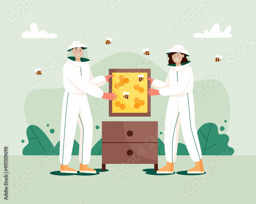 Man and woman in hat and protective uniform with a honeycomb frame and beehive. Beekeeping workers in uniforms.