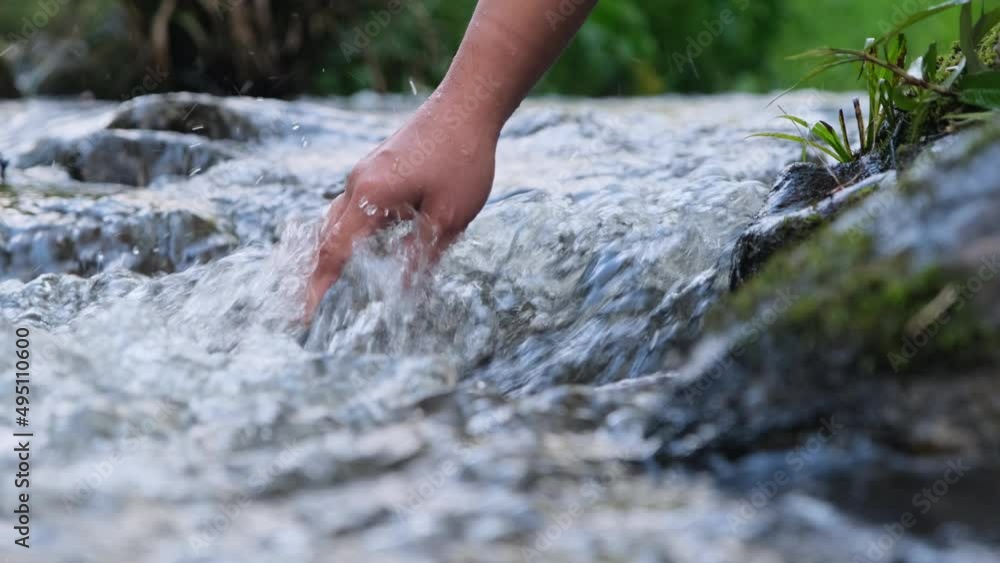 Female hand touching cold water in the river. Trekking woman stands on a rock and touches a stream with her hands. Close-up of the hand Female hand touching cold water in the river. Trekking woman stands on a rock and touches a stream with her hands. Close-up of the hand