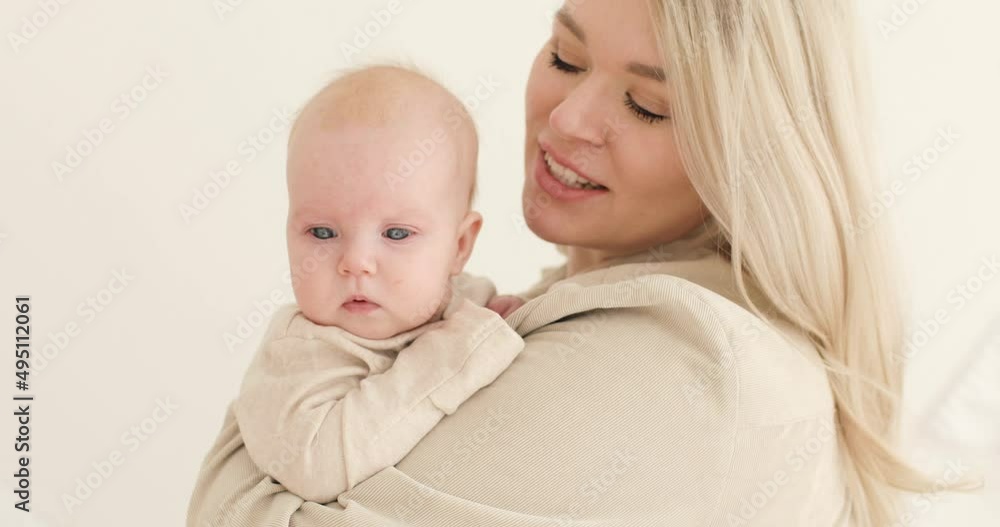Portrait of a young mother, blonde, holding a newborn baby in her arms indoors. The woman smiles. Parenting. The concept of motherhood. Portrait of a young mother, blonde, holding a newborn baby in her arms indoors. The woman smiles. Parenting. The concept of motherhood.
