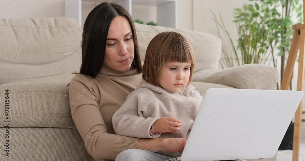 Little daughter sitting with mother busy working on laptop at home Little daughter sitting with mother busy working on laptop at home