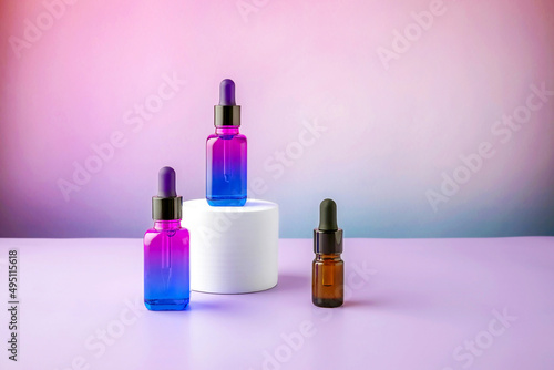 multi-colored bottles with a pipette for cosmetics on the podium on a color gradient background