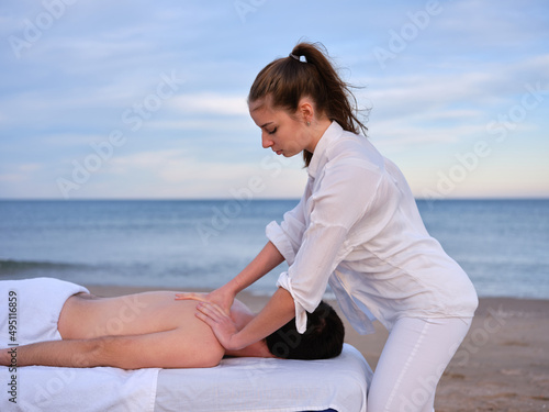 Chiromassage therapist woman giving a back massage to young man on a beach in Valencia.