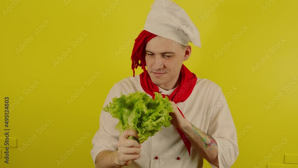 Man with red dreadlocks holds lettuce leaves. Confident young cook in white shirt and red tie holding lettuce leaves