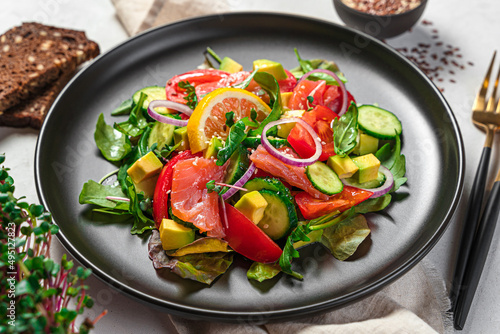 Healthy vegetable salad with salmon and avocado on a gray background.