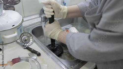 a woman cleans a clogged sink with a plunger