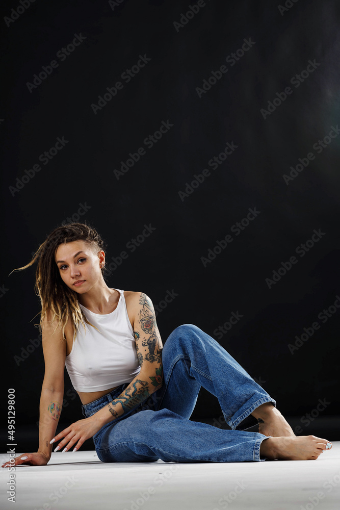 tattooed girl in jeans and a white tank top on a black background tattooed girl in jeans and a white tank top on a black background
