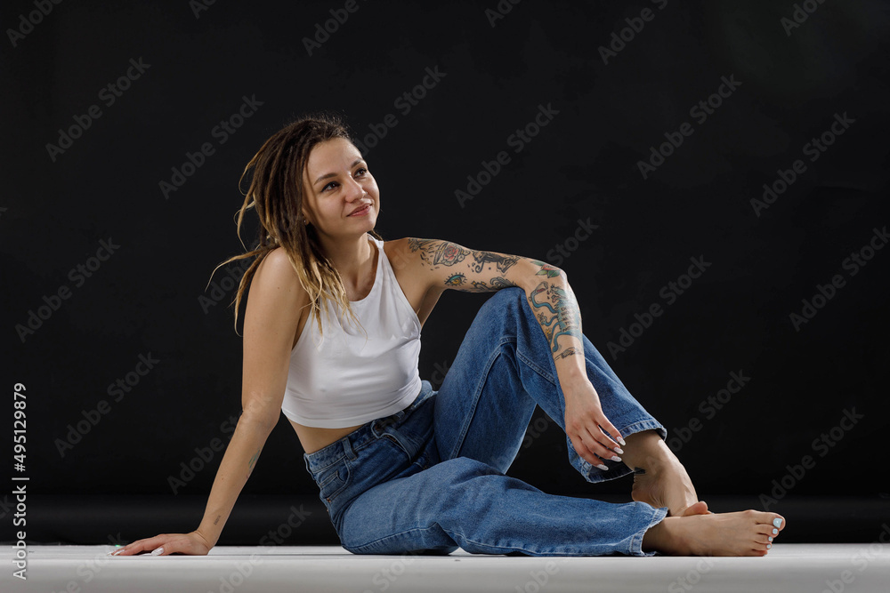 tattooed girl in jeans and a white tank top on a black background