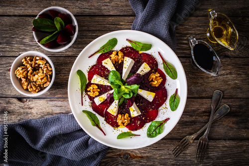 Tableau sur toile Beetroot carpaccio with goat cheese, greens and walnuts on wooden background