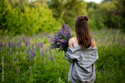 young beautiful girl holds in her hands spring lupine flowers and turned her back