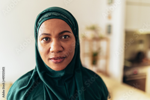 Photography Muslim woman in hijab looking at camera at home.