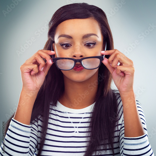 Checking for dirt on her glasses. Shot of a young woman posing against a grey background.