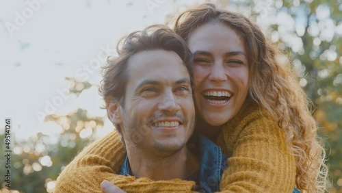 Portrait of happy loving couple with man giving woman piggyback and hugging her in autumn park - shot in slow motion 