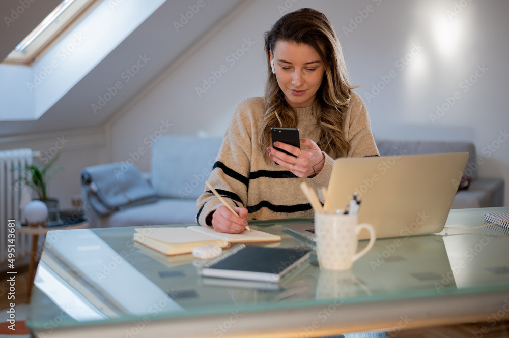 Woman using smartphone while working at home and using a laptop