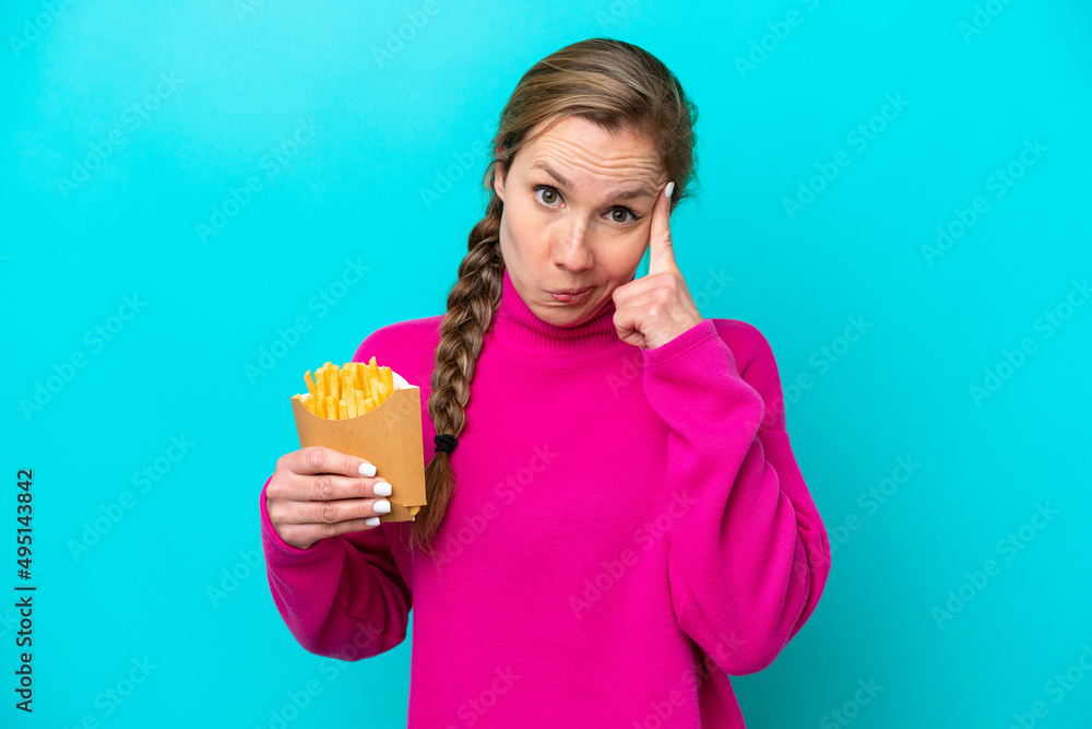 Young caucasian woman holding fried chips isolated on blue background thinking an idea Young caucasian woman holding fried chips isolated on blue background thinking an idea