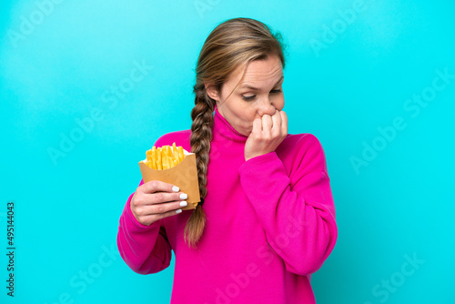 Young caucasian woman holding fried chips isolated on blue background having doubts