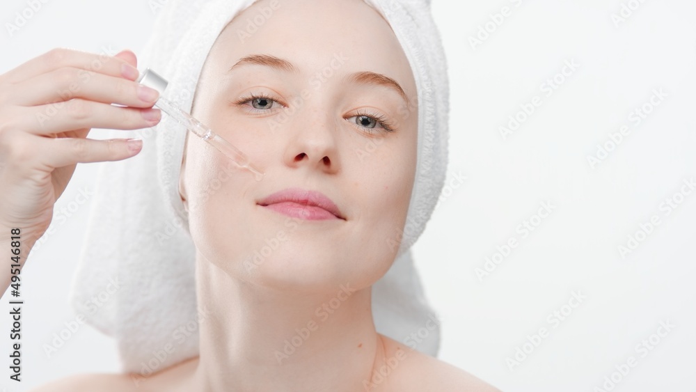 Big close-up shot of young Caucasian woman with a head towel applies face serum on white background | Face care serum commercial concept