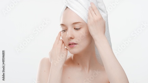 Beauty portrait of young ginger woman with towel on her head who touches her face with both hands on white background