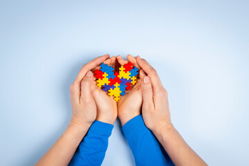 World autism awareness day concept. Adult and child hands holding puzzle heart on light blue background. Top view