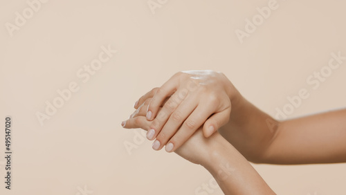 Horizontal close-up shot of female hands are rubbed and interlocked on beige background   Dry hands prevention concept