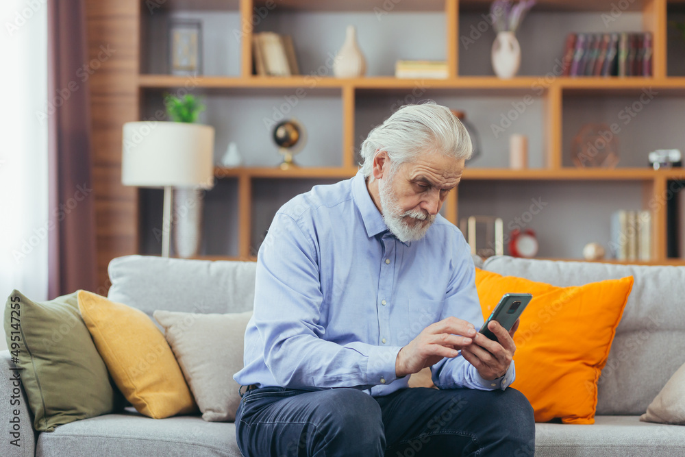 Senior man at home sitting on sofa looking at phone screen, talking on video call with family Senior man at home sitting on sofa looking at phone screen, talking on video call with family