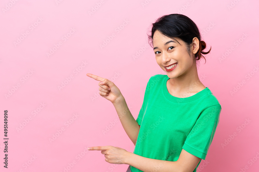 Young Vietnamese woman isolated on pink background pointing finger to the side and presenting a product Young Vietnamese woman isolated on pink background pointing finger to the side and presenting a product