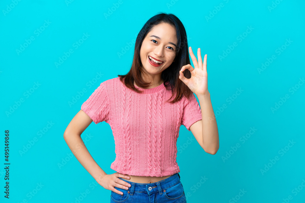Young Vietnamese woman isolated on blue background showing ok sign with fingers Young Vietnamese woman isolated on blue background showing ok sign with fingers