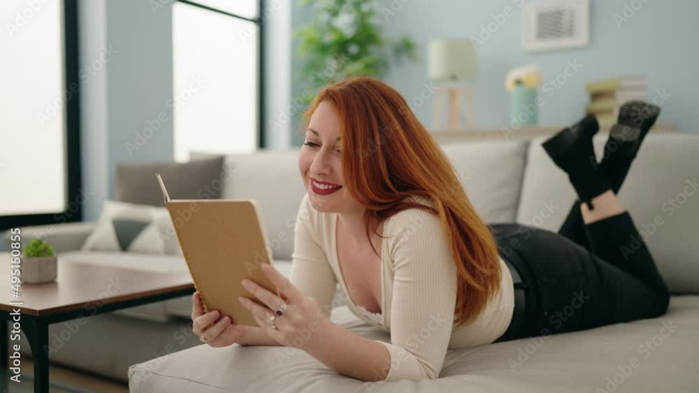 Young redhead woman reading book lying on sofa at home Young redhead woman reading book lying on sofa at home