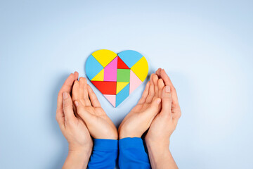 World autism awareness day concept. Woman and child hands holding puzzle heart on light blue background. Top view