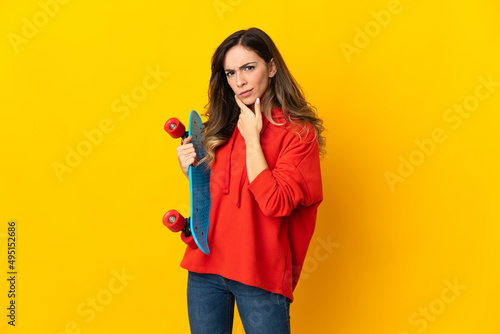 Young caucasian woman isolated on yellow background with a skate and looking lateral
