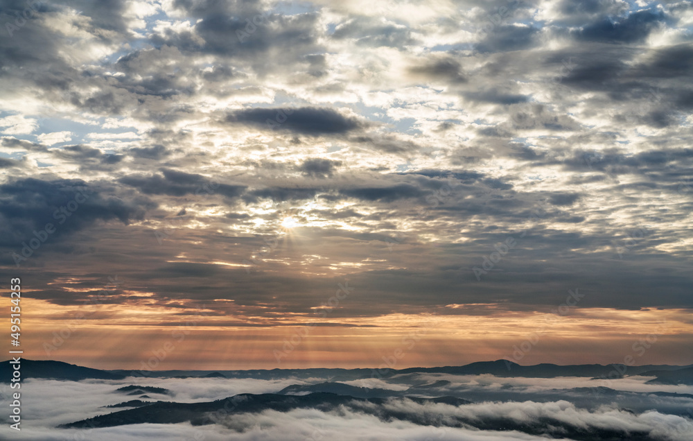 Sunrise and cloudy sky over the mountains. The tops of the mountains in the fog. Cloud formation.