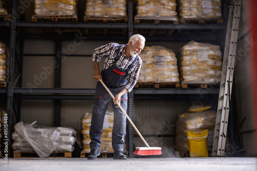  A senior factory worker is brooming factory hall. photo