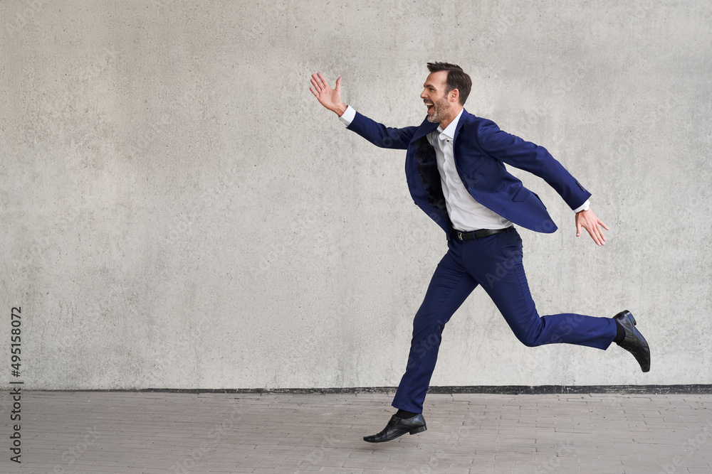 Picture of businessman in suit running against concrete wall