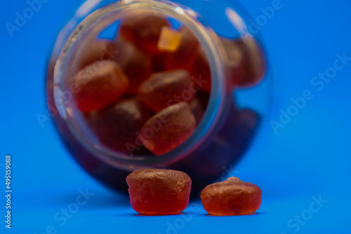 Plastic bottle full of gummy vitamins sideways with gummies falling out in front of blue background.