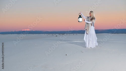 Attractive woman in white dress holding light on white sands against sunset pink sky. White sands. New Mexico. United States of America