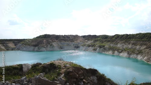 Waste rock dumps of ilmenite quarry next to quarry lake with blue water, vertical aerial view. Blue water lake that originated on the site of a quarry where clay, sand and minerals are mined. photo