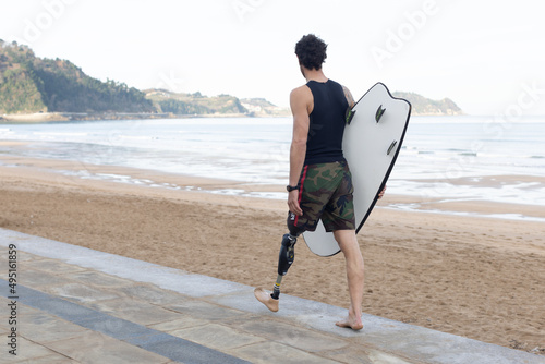 Caucasian surfer man strolling along the edge of the beach with an artificial leg