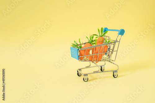Easer creative concept of shopping basket full of carrots for rabbits. Pastel yellow background.