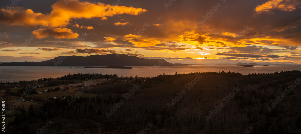 Aerial Panoramic View of Orcas Island During a Dramatic Sunset. Seen from neighboring Lummi island looking across Rosario Strait at the sun dropping below the dynamic cloudscape.