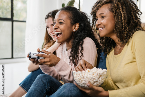 United multiracial young women playing video games wit console at home - Diverse female friends laughing having a great time together - Friendship and entertainment concept photo