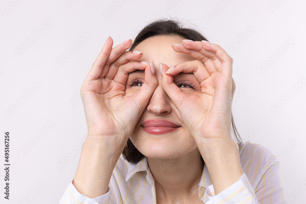 Close up portrait of attractive quirky young woman making binoculars with hands showing ok gesture on white studio background. Close up portrait of attractive quirky young woman making binoculars with hands showing ok gesture on white studio background.