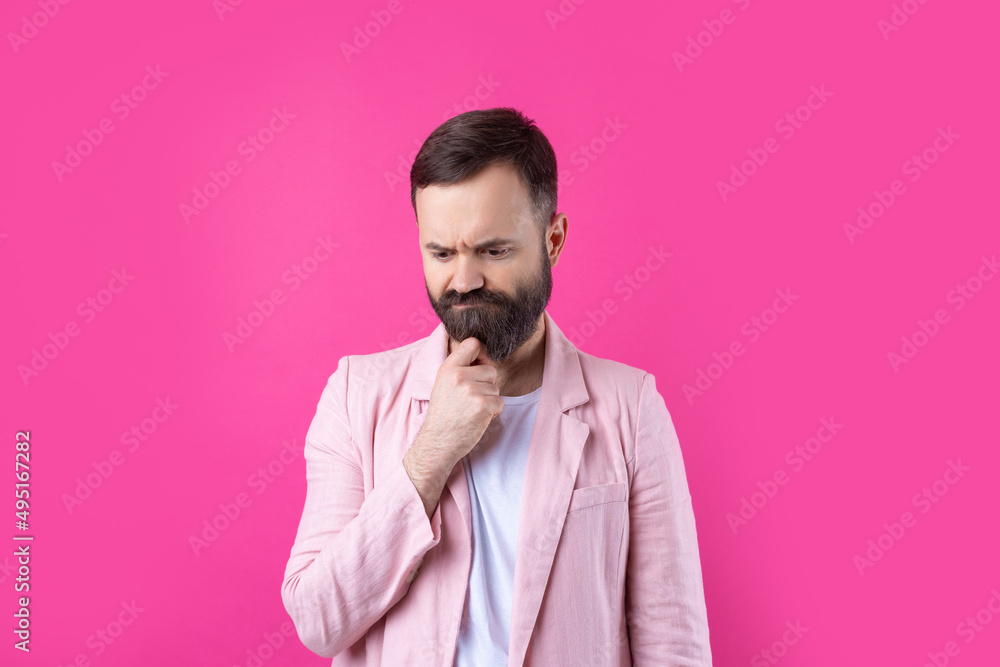 Handsome man with a beard in a pink jacket is thinking over an isolated red background.
